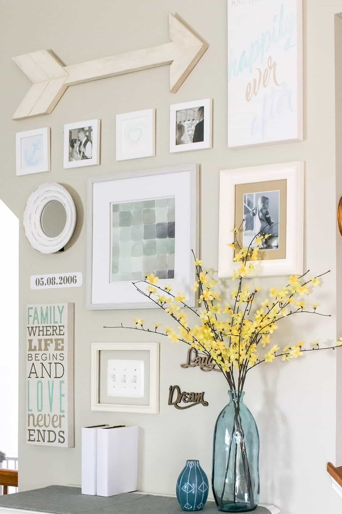 Gallery wall with a DIY arrow wall decoration, framed art, and glass vase with yellow flowers. 