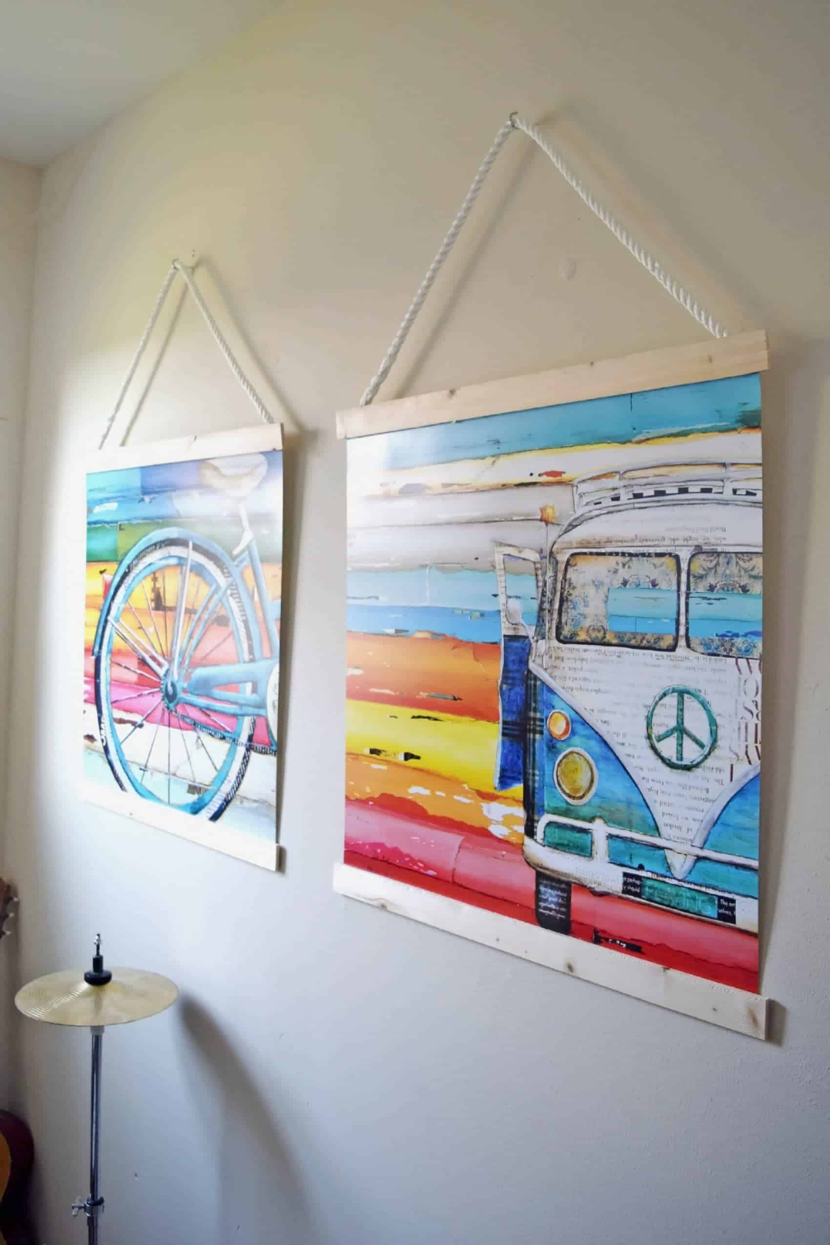 DIY wooden frames on white hanging ropes with colorful bicycle and VW bus art on white wall. 