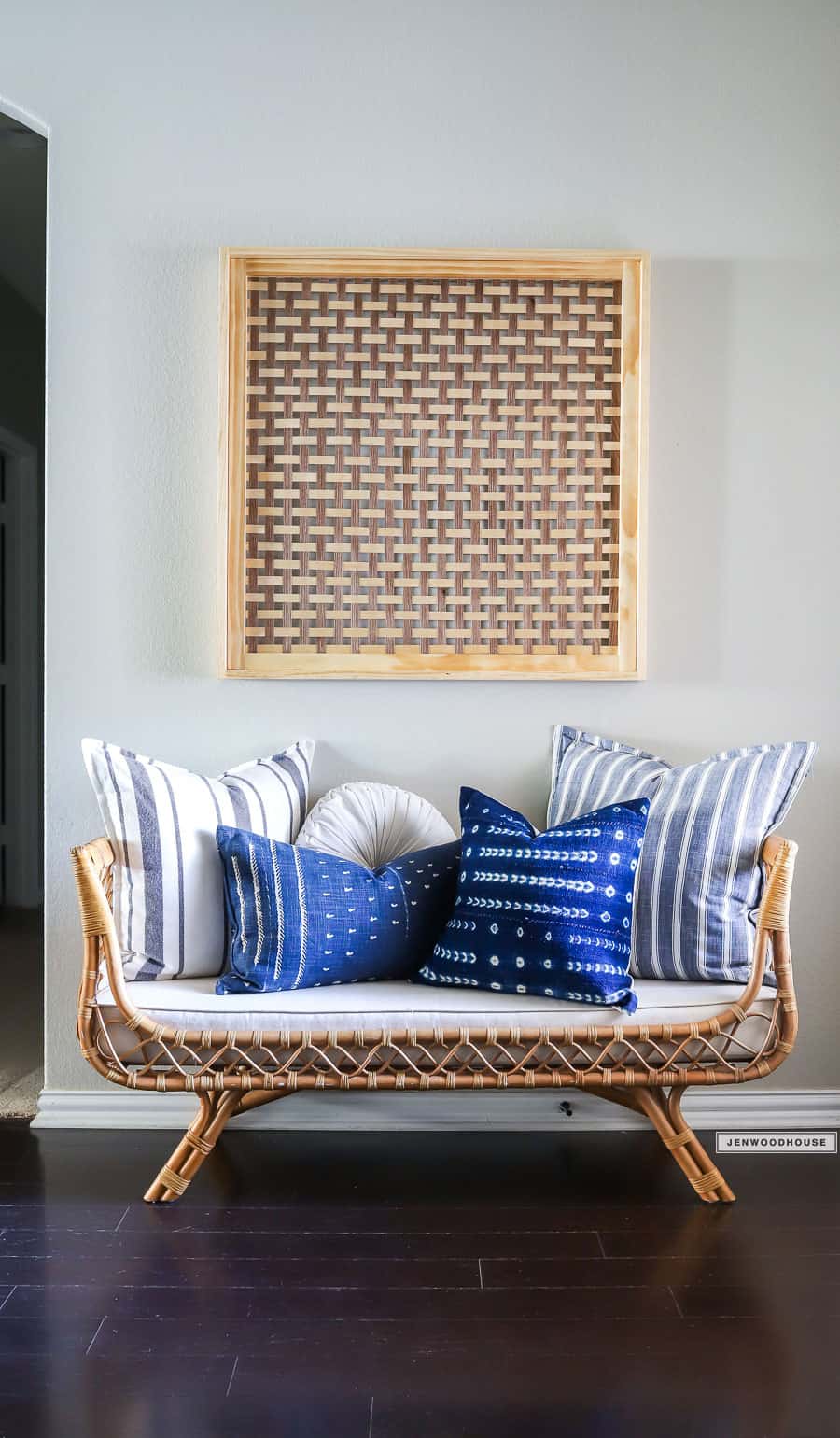 Natural basket weave statement wood wall art against neutral wall hung above wicker settee with blue and white pillows.