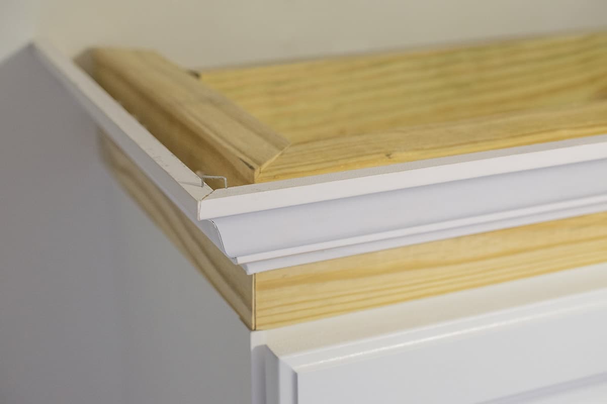Corner of top of white cabinet with framing piece and trim attached. 