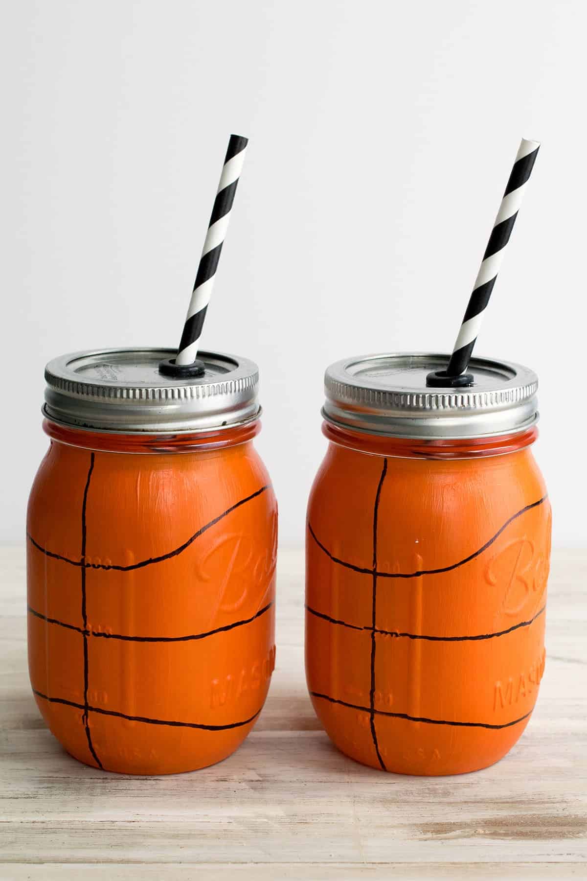 Hand painted basketball mason jars with metal lids and black and white paper straws. 