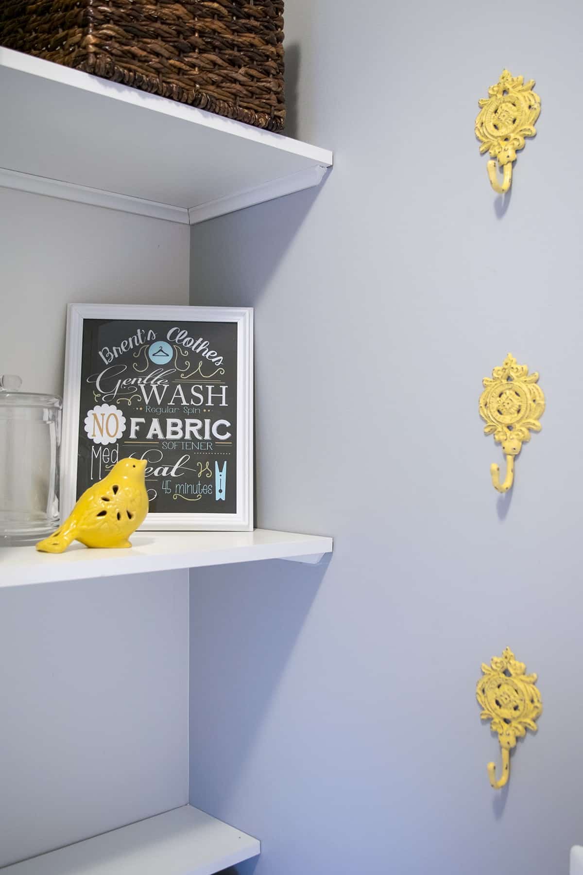 White shelf next to soft gray wall with 3 decorative yellow hooks in laundry room. 