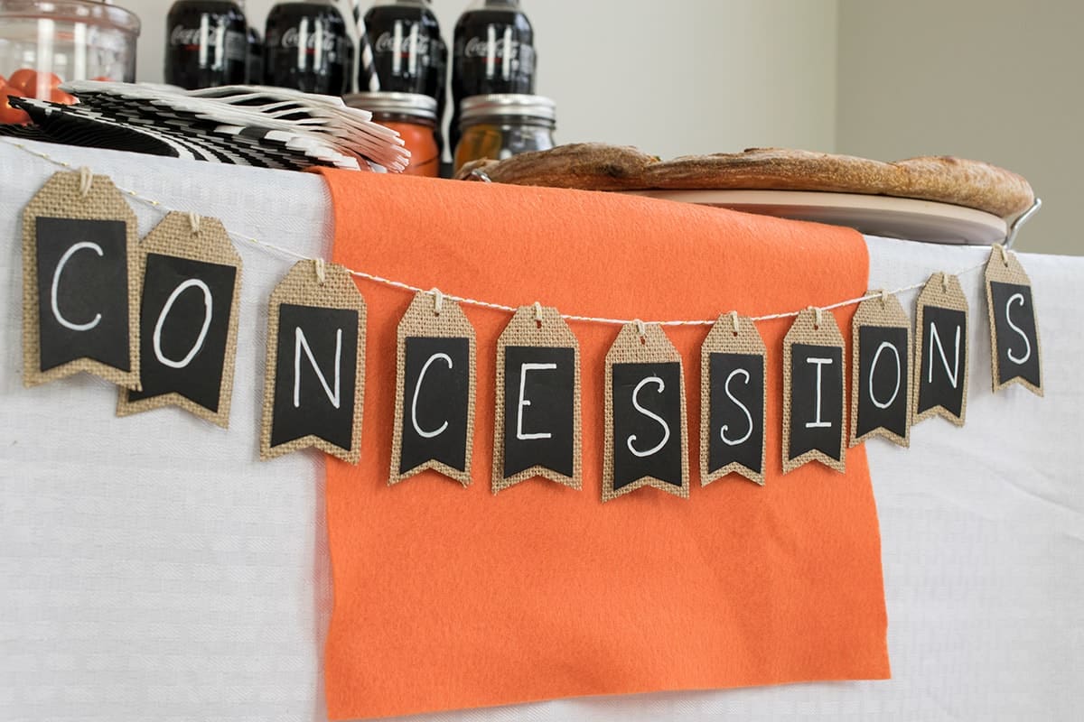 White party table with orange table runner and black concessions banner on burlap tags. 