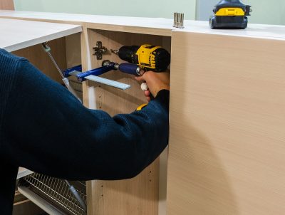 Man using a drill and clamps to attach wall cabinets together