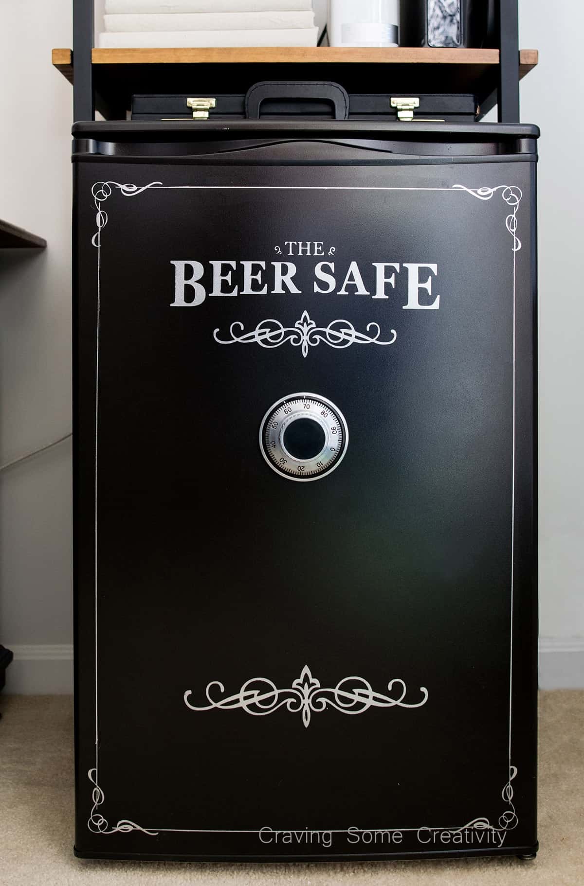 Mini fridge DIY makeover painted black with vinyl details to look like a miniature gun safe, complete with safe dial. 