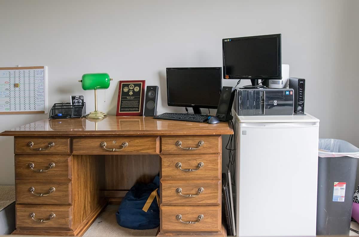 Cluttered office with old antique desk and mini refrigerator before makeover. 