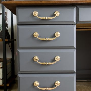 Gray painted desk with brass handles and a wood top.