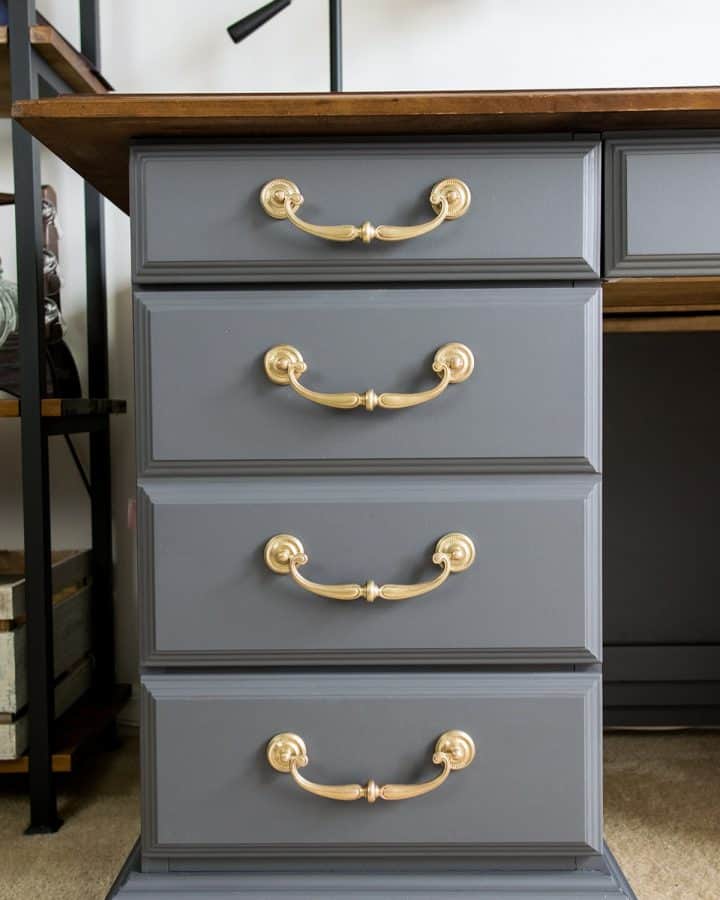 Gray painted desk with brass handles and a wood top.