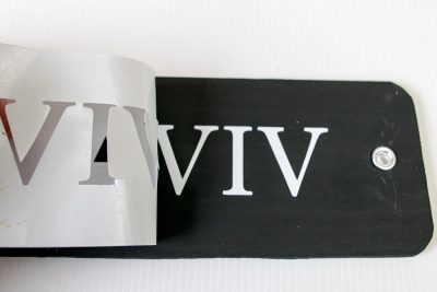 Peeling back vinyl lettering from a black name plate.