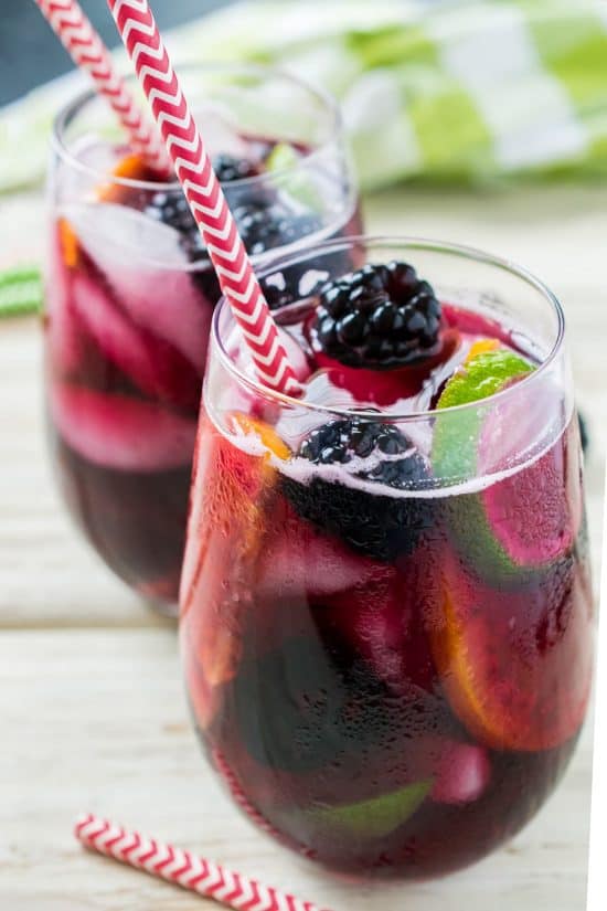 Two glasses of blackberry sangria with straws on a wood background.
