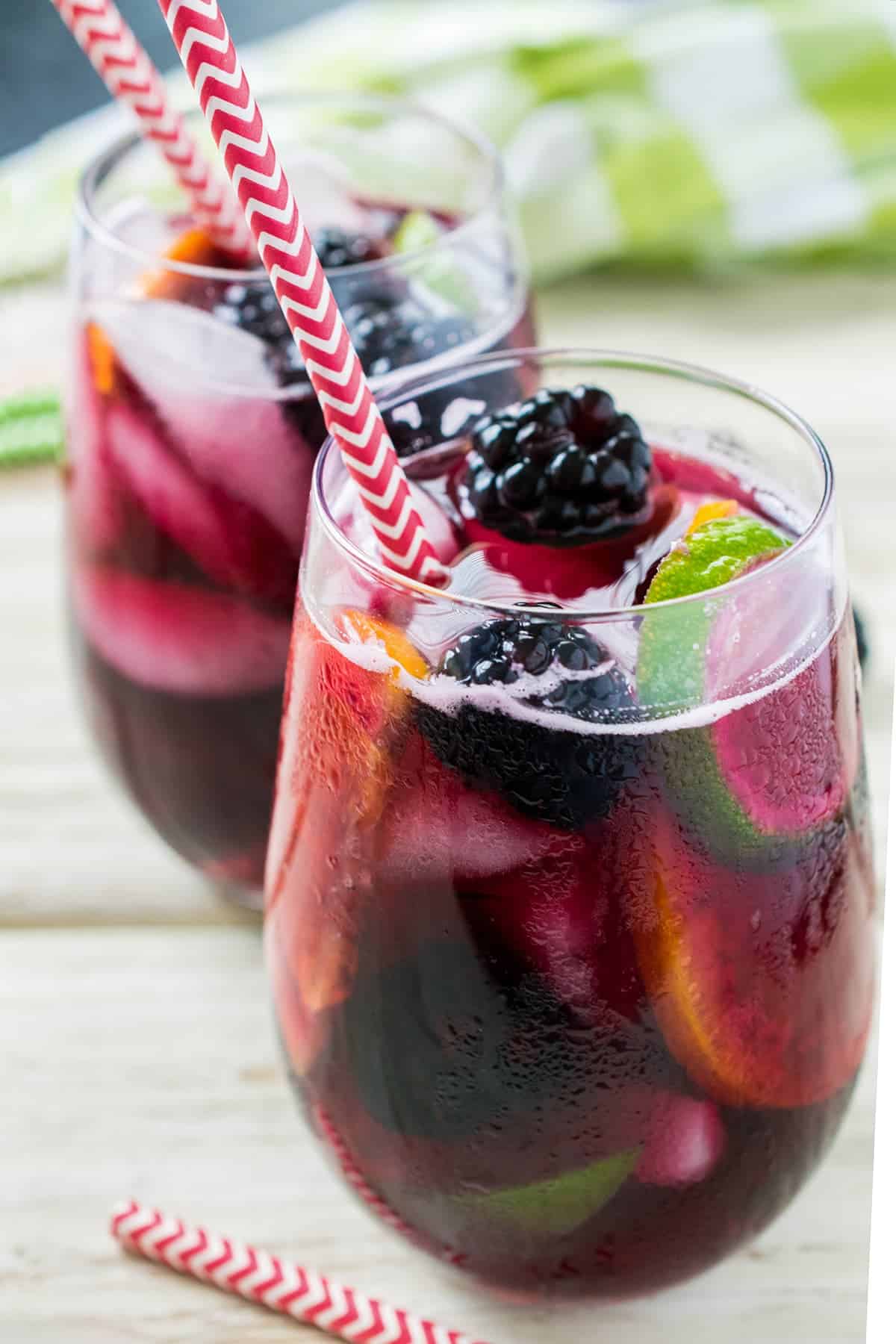 Two stemless wine glasses filled with blackberry sangria over ice with oranges, lime wheels, and fresh blackberries. 