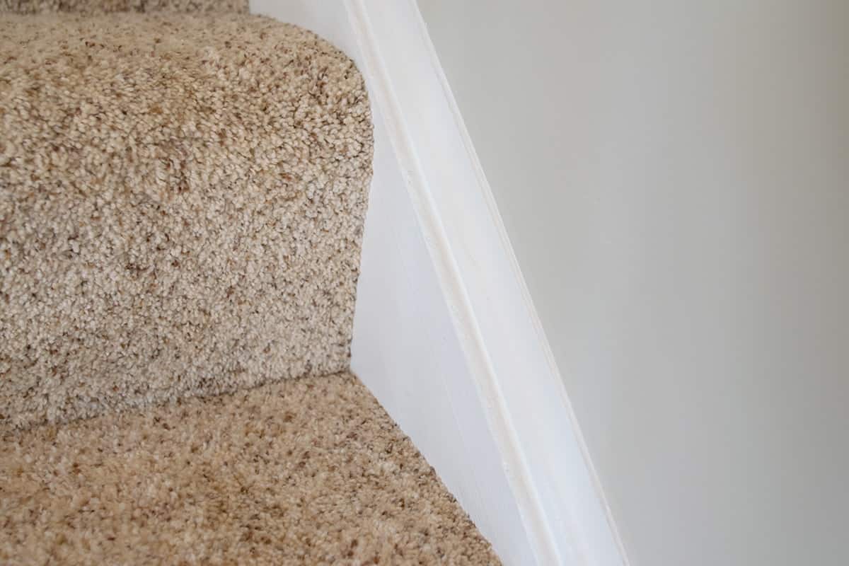 Carpeted stairwell with white baseboard and clean caulking lines 