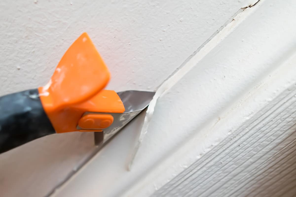 Orange caulk remover tool used to scrape away old, damaged caulk on baseboard. 