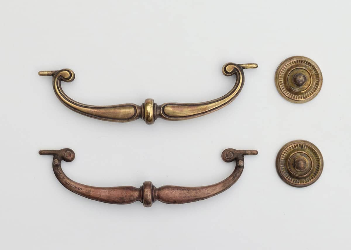 The back and front of antique brass desk hardware after cleaning with vinegar paste.