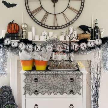 Spooky Halloween mantle with dessert buffet in front. Decorations include ravens, gravestones, a clock, and candles.