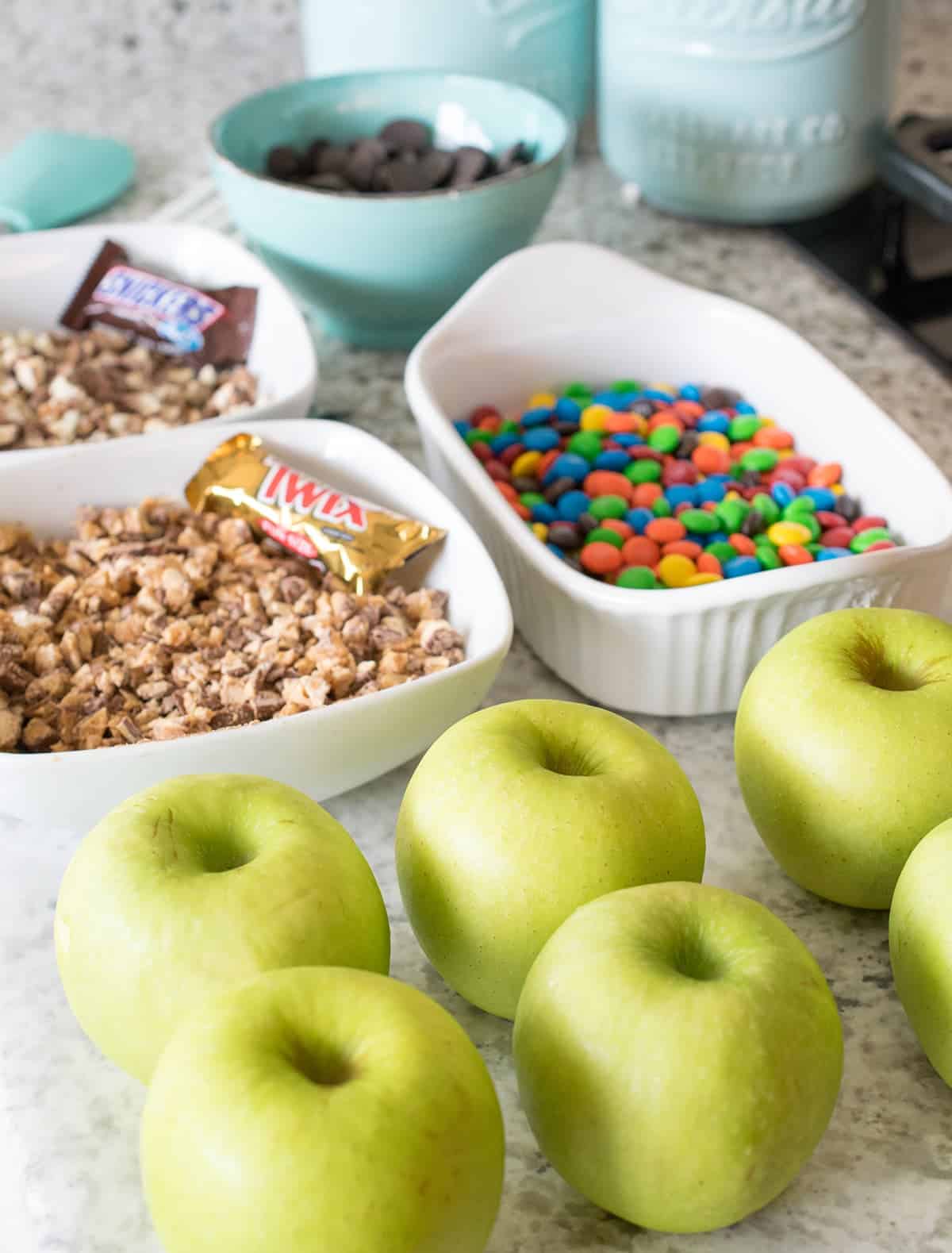 Candy apple rolling station with fresh green apples, assorted candy dishes with m&m's, crushed twix candy bars, snickers, and dipping chocolate.