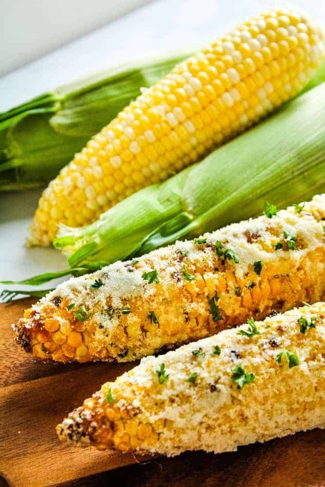 Parmesan air fryer corn on the cob in front of fresh ears of corn.