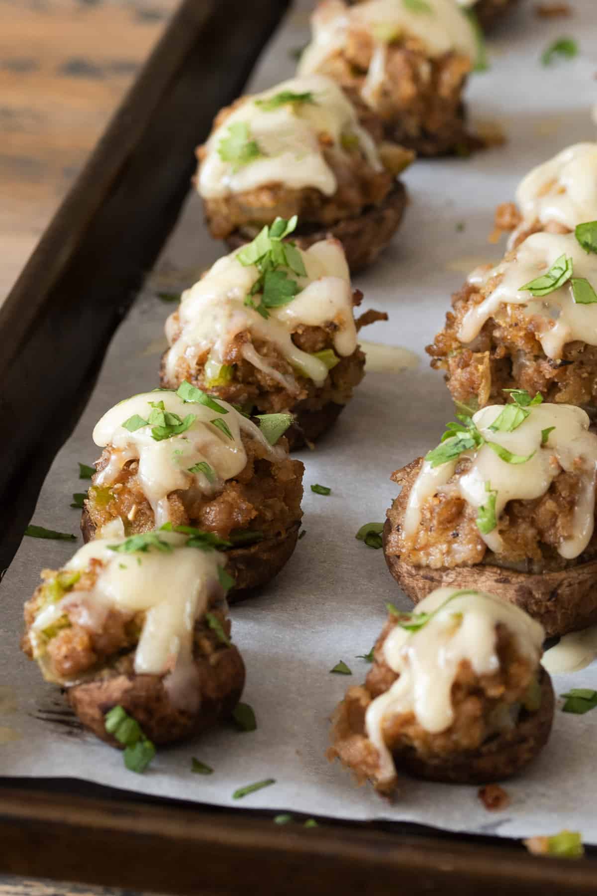 Sausage stuffed mushrooms on a sheet pan topped with swiss cheese and parsley.