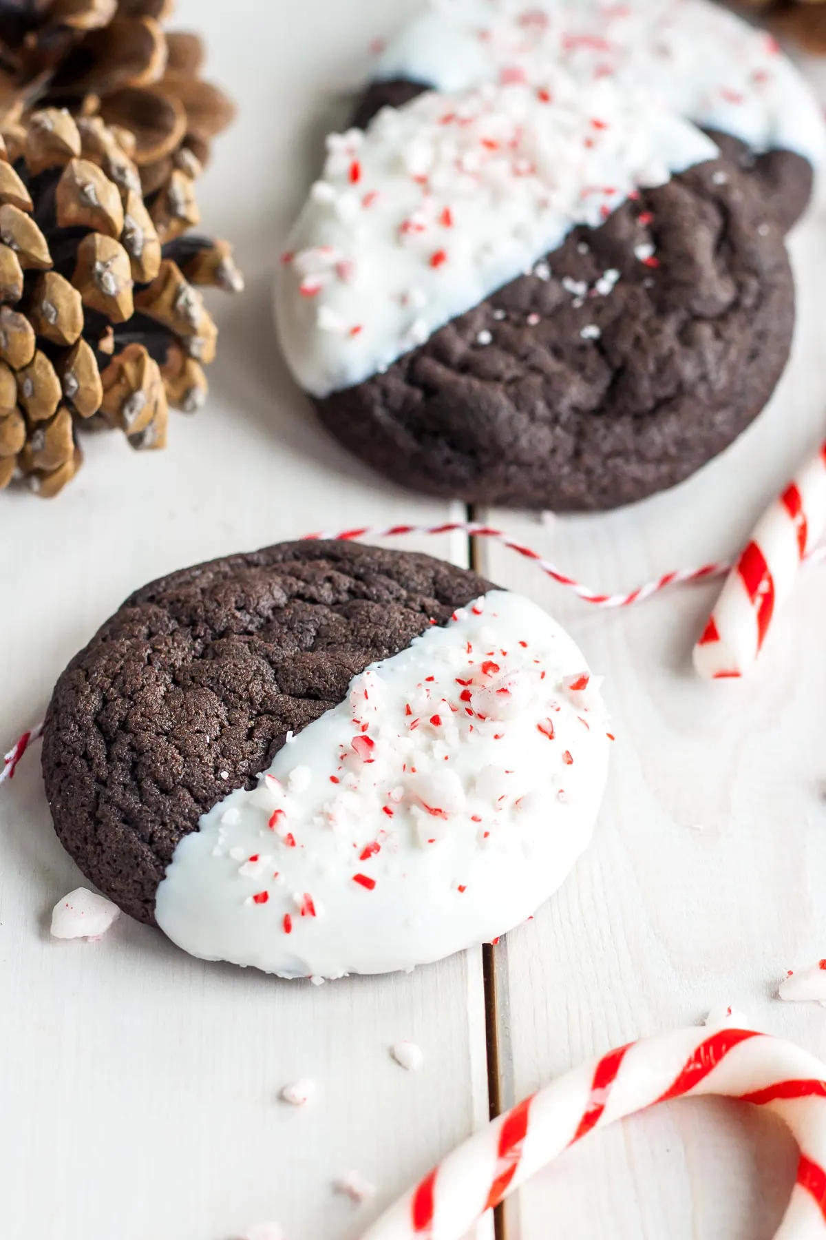 Dark chocolate peppermint cookies dipped in white chocolate on a white wood background with candy canes around them.