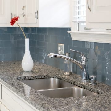 Kitchen with blue tile backsplash, white cabinets, and gray granite countertops.