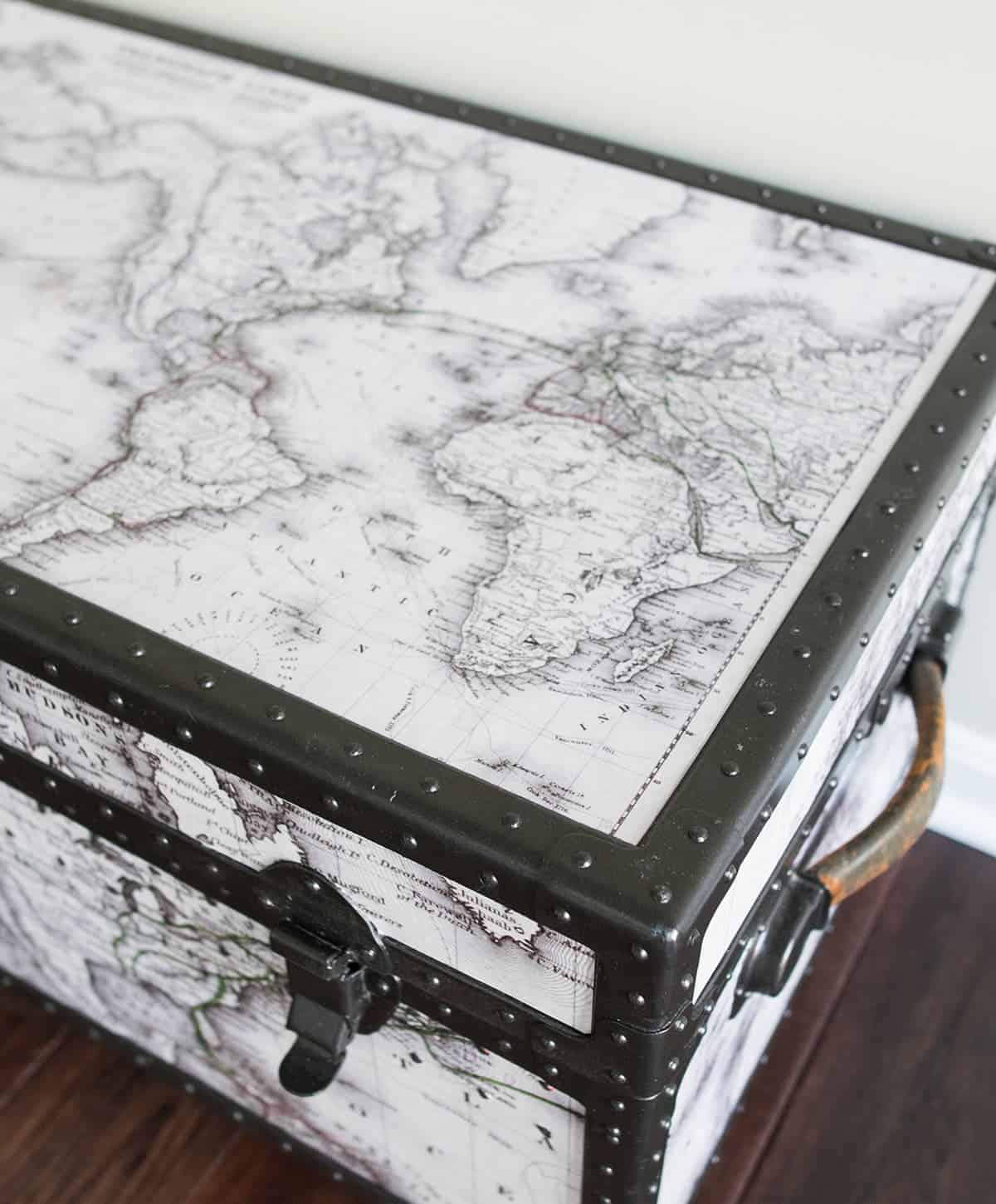 Closeup of a metal steamer trunk makeover with black and white maps and metal rivets painted black.