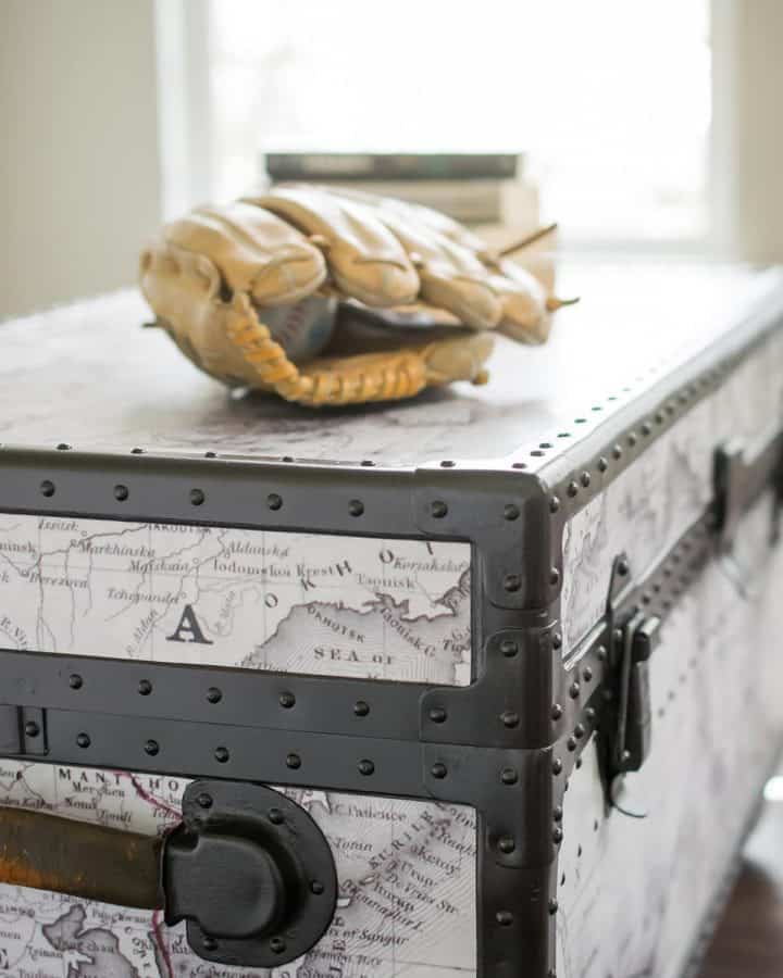 Side shot of antique trunk makeover with rivets, metal sides, and map added. Baseball glove on top of footlocker.