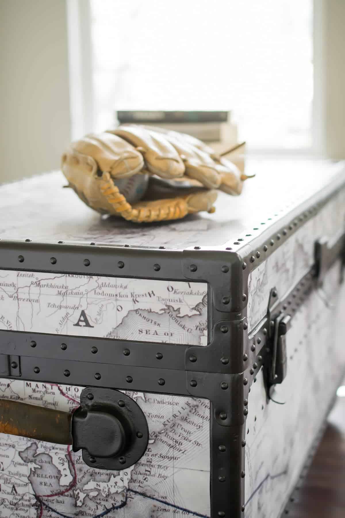 Side shot of antique trunk makeover with rivets, metal sides, and map added. Baseball glove on top of footlocker.