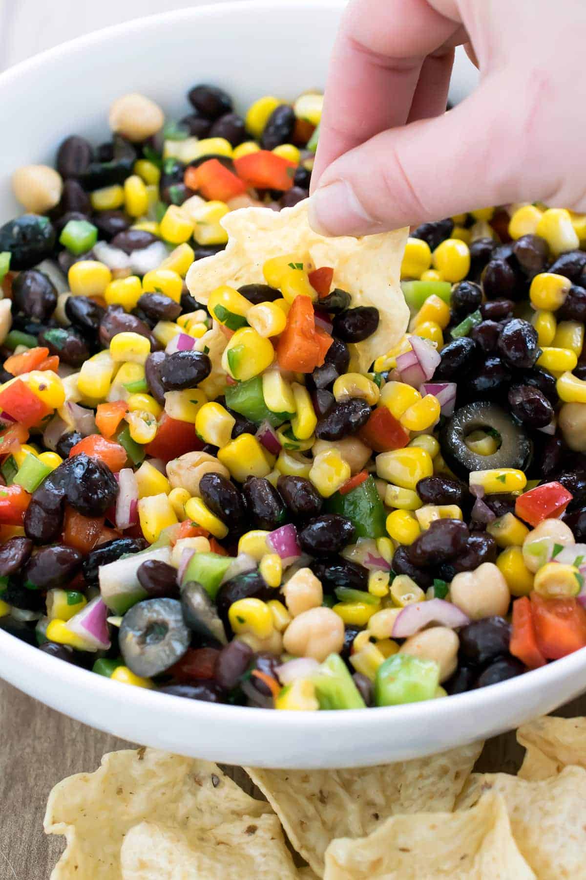 Light and fresh Cilantro black bean and corn salsa in bowl  while a hand reahes in to scoop with tortilla chip.