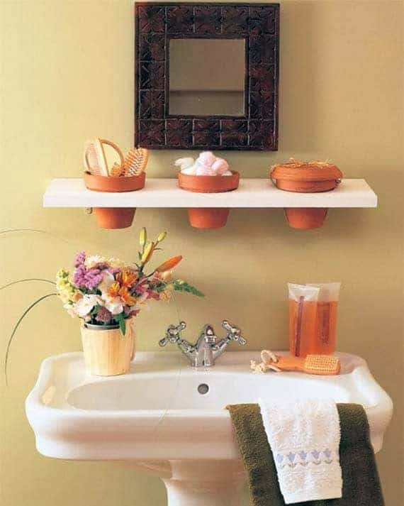 Mini recessed clay flower pots set in white floating shelf on bathroom wall for storage. 