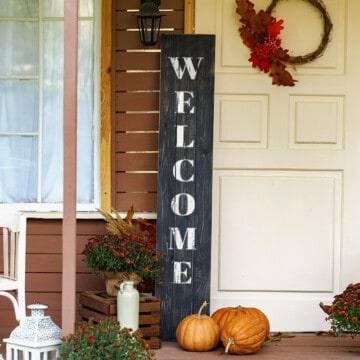 Black DIY welcome sign on front porch decorated for fall.