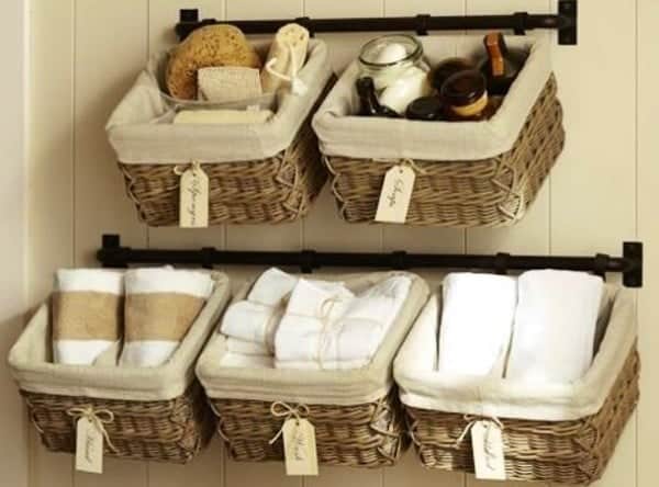 Cast iron rods mounted in bathroom with lined hanging baskets storing linens and toiletries. 