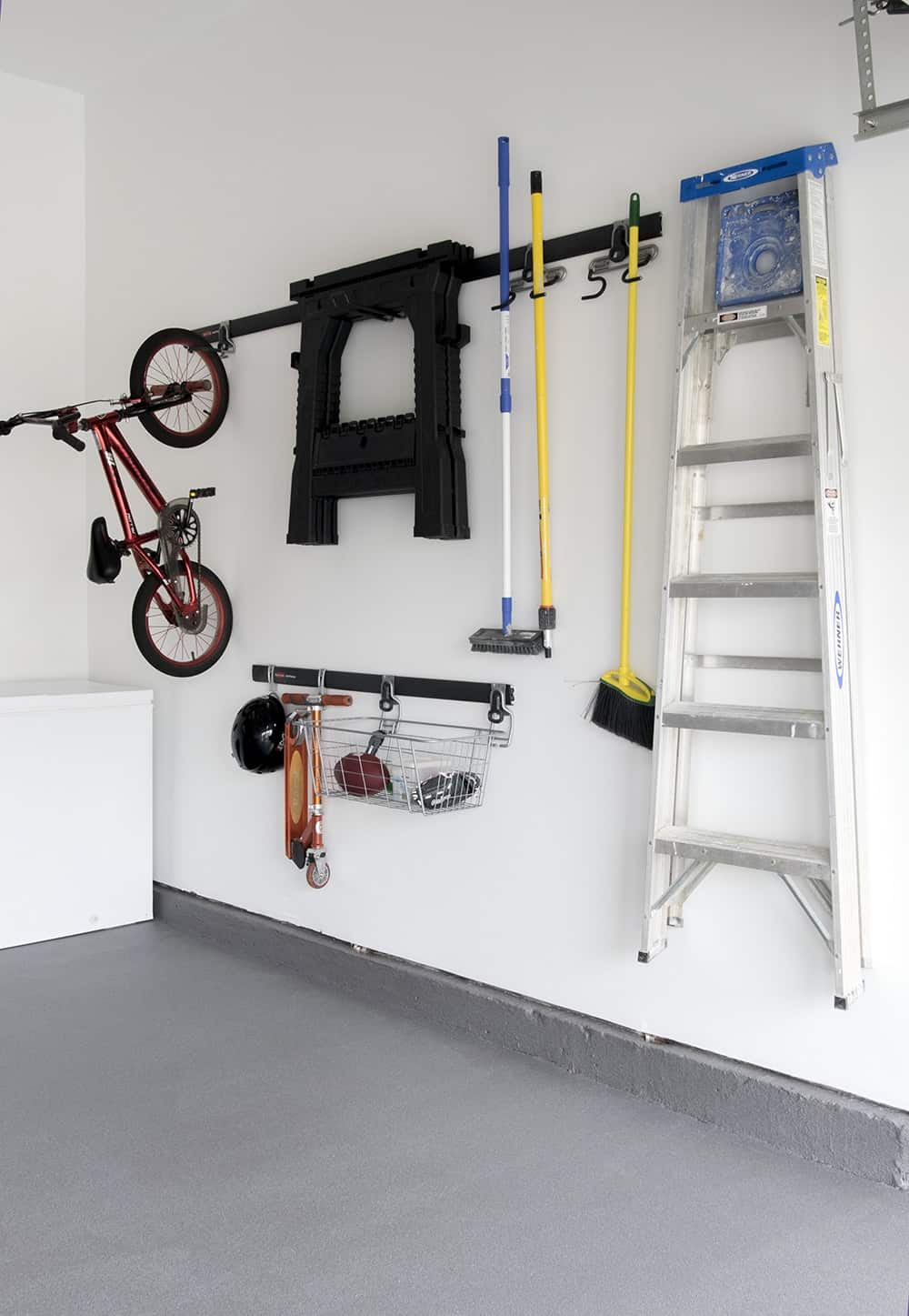 Non- slip floor in residential garage below organized hanging wall with ladders, toys, and cleaning supplies. 