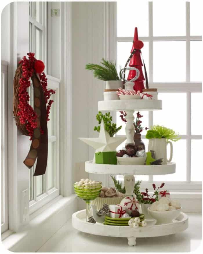 Tiered white tray with small Christmas candies, greenery and baubles.