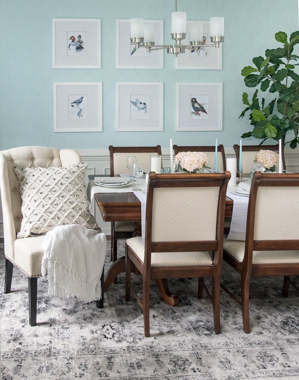 Classic chic dining room with area rug, natural accents, gray curtains, black lanterns, and soft blue walls. 