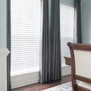 Two windows with blinds closed and grey curtains on either side.