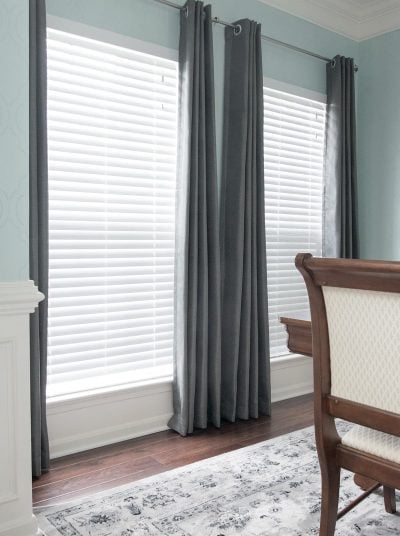 Two windows with blinds closed and grey curtains on either side.
