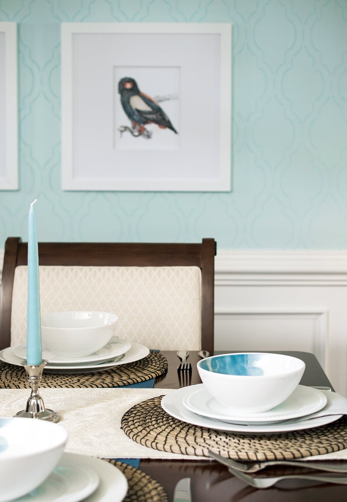 Dining room place settings. White table runner with place settings with and wicker placemats, white dinnerware with blue accents.