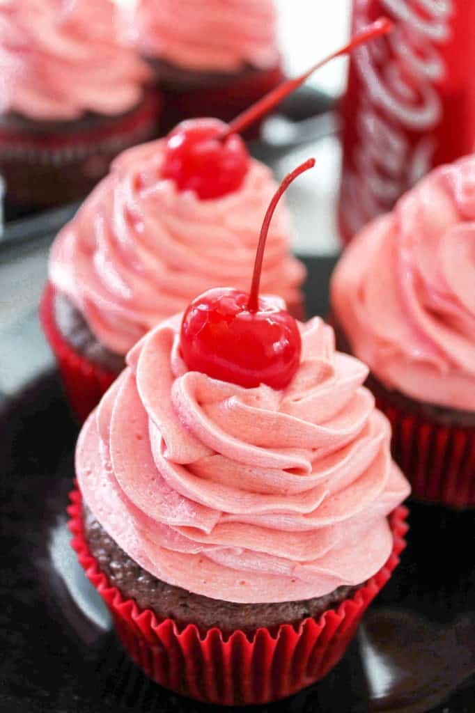 Delicious cherry coke cupcakes with vibrant pink cherry frosting, topped with a cherry 