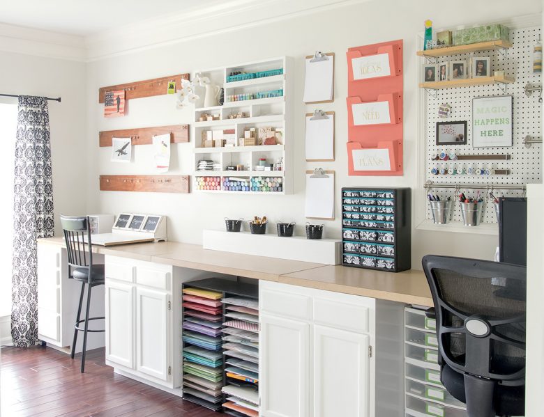 Colorful craft room with white walls and white cabinets with craft supplies on the wall and a pegboard.
