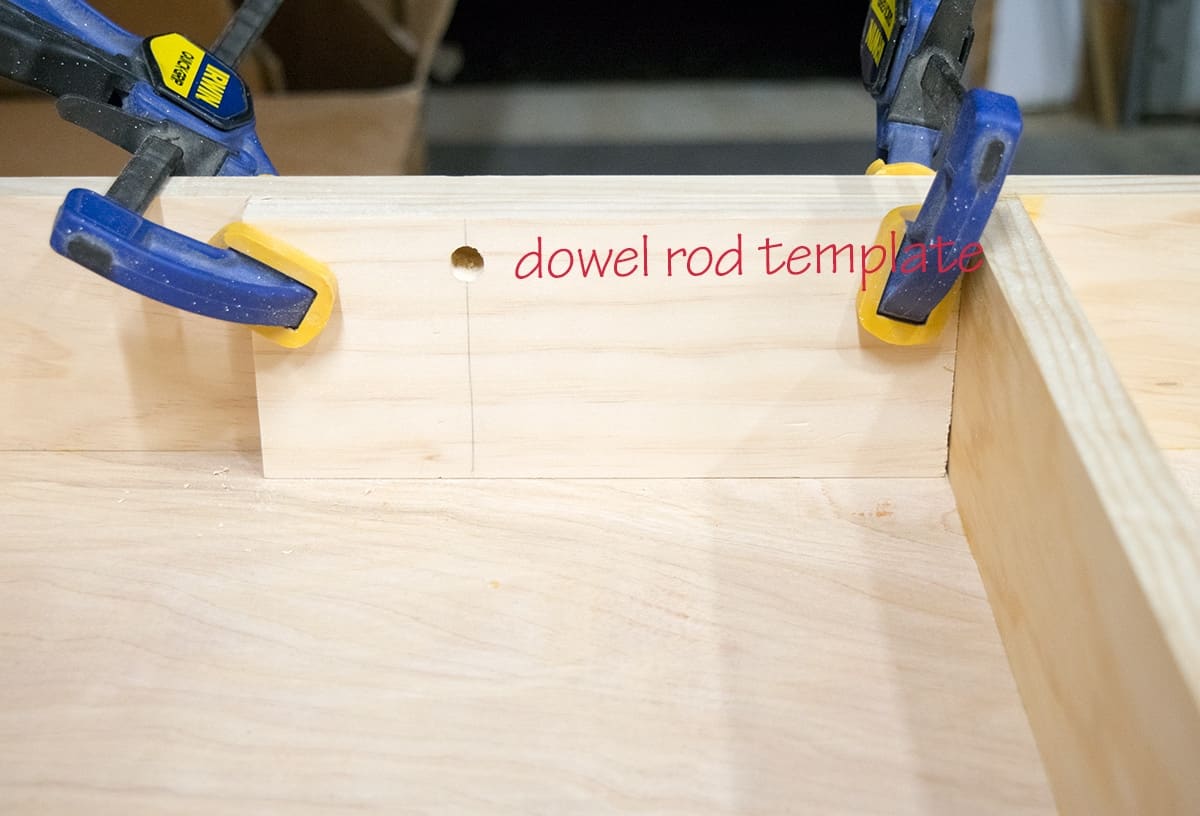 Dowel rod jig template placed with clamps between shelves.