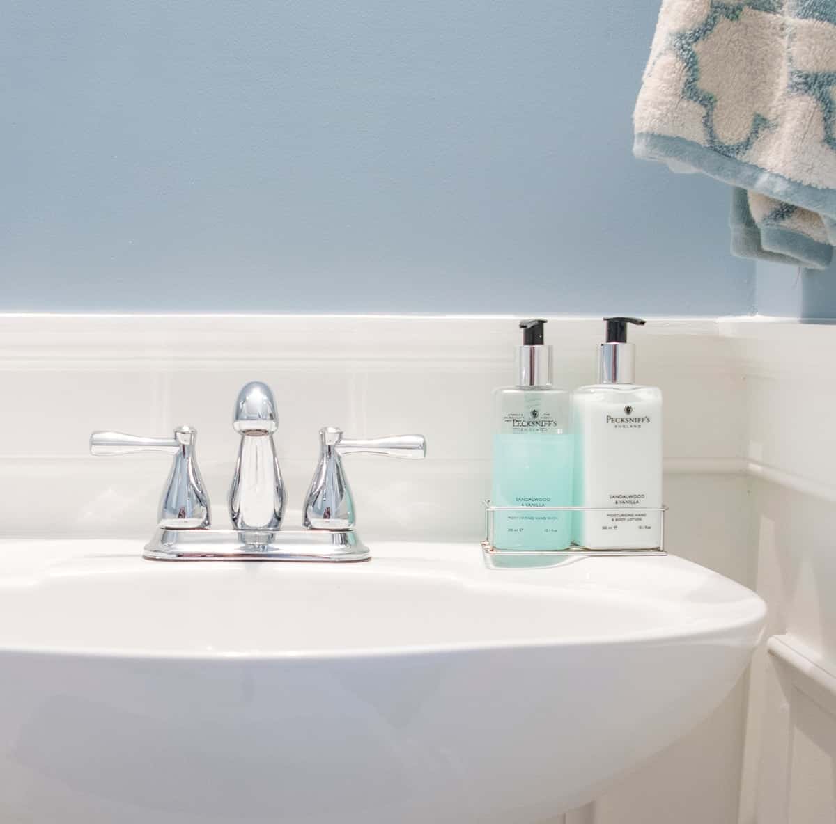 Polished white freestanding sink with chrome faucet with light blue wall and white wainscoting