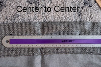 A ruler in front of a curtain to measure the distance between holes.