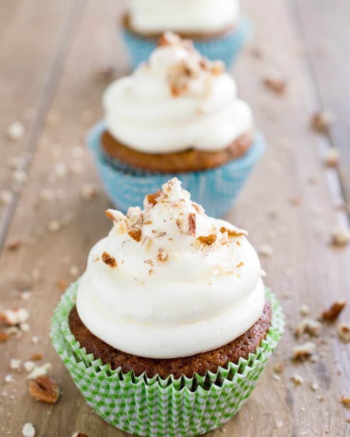 Three cupcakes with homemade cream cheese frosting and sprinkled with nuts.