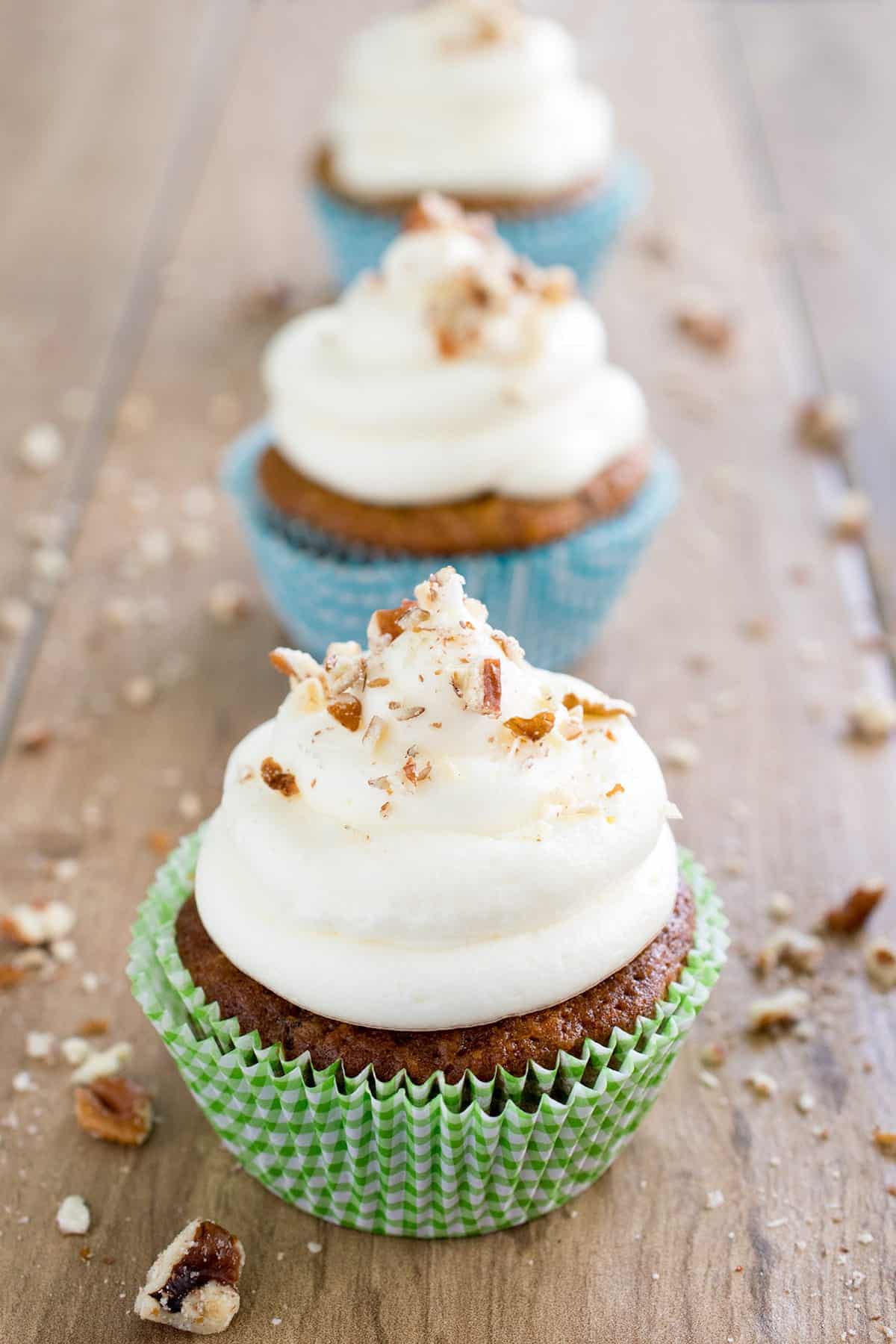 Carrot cake cupcakes with fluffy cream cheese frosting topped with chopped walnuts on wooden cutting board 