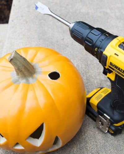 Carvable orange pumpkin next to drill with hole drilled out for stacking on wooden dowel.