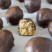 Rows of chocolate covered peanut butter balls on sheet of wax paper. Cookie in the center is sliced in half to reveal crispy peanut butter center.