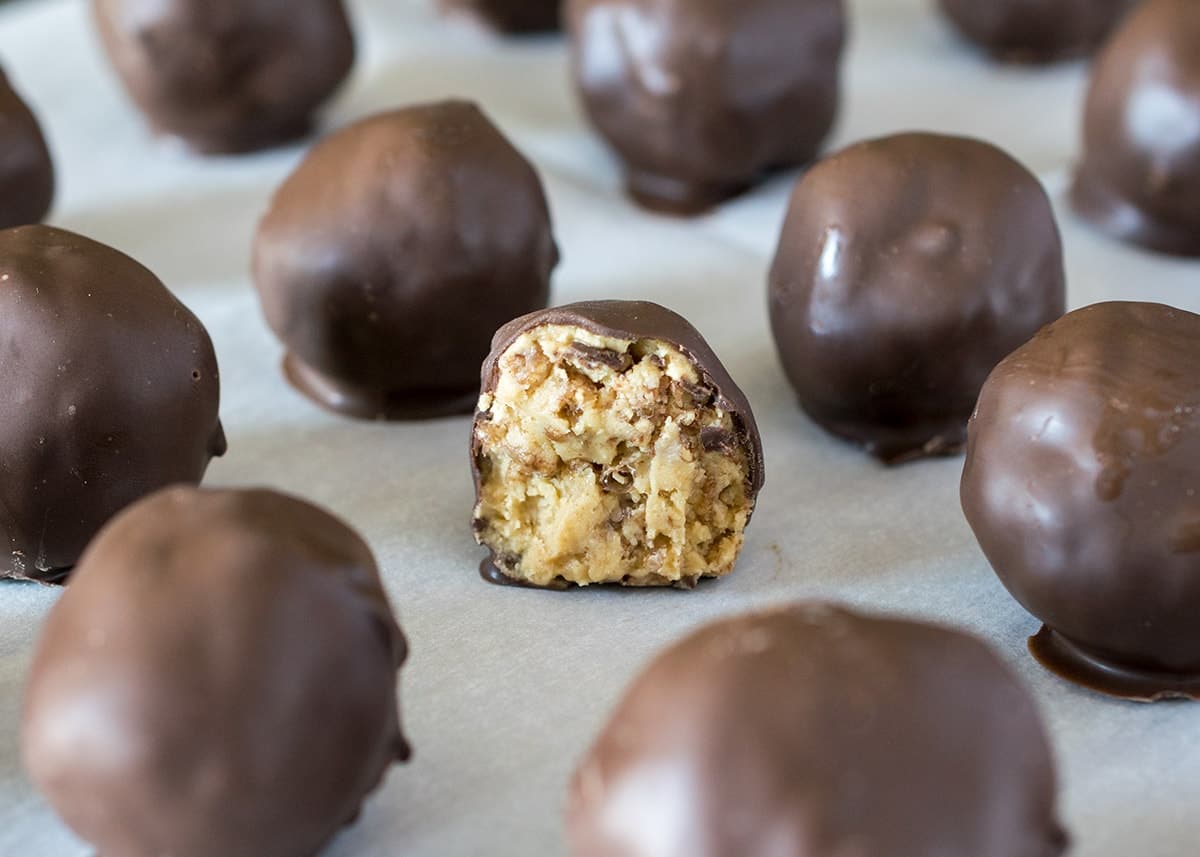 Rows of chocolate covered peanut butter balls on sheet of wax paper. Cookie in the center is sliced in half to reveal crispy peanut butter center.