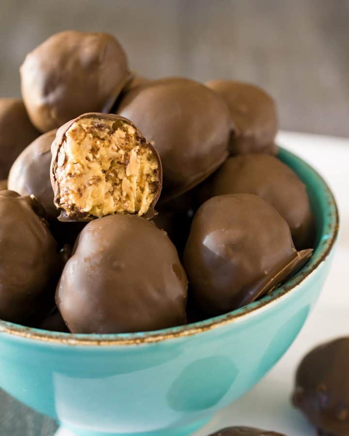 A bowl of peanut butter balls with one bite taken out to show inner texture.