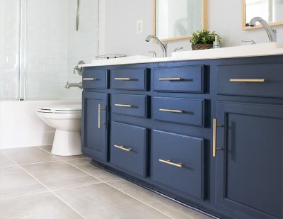 Midnight blue vanity with brass handles in a grey and white bathroom.