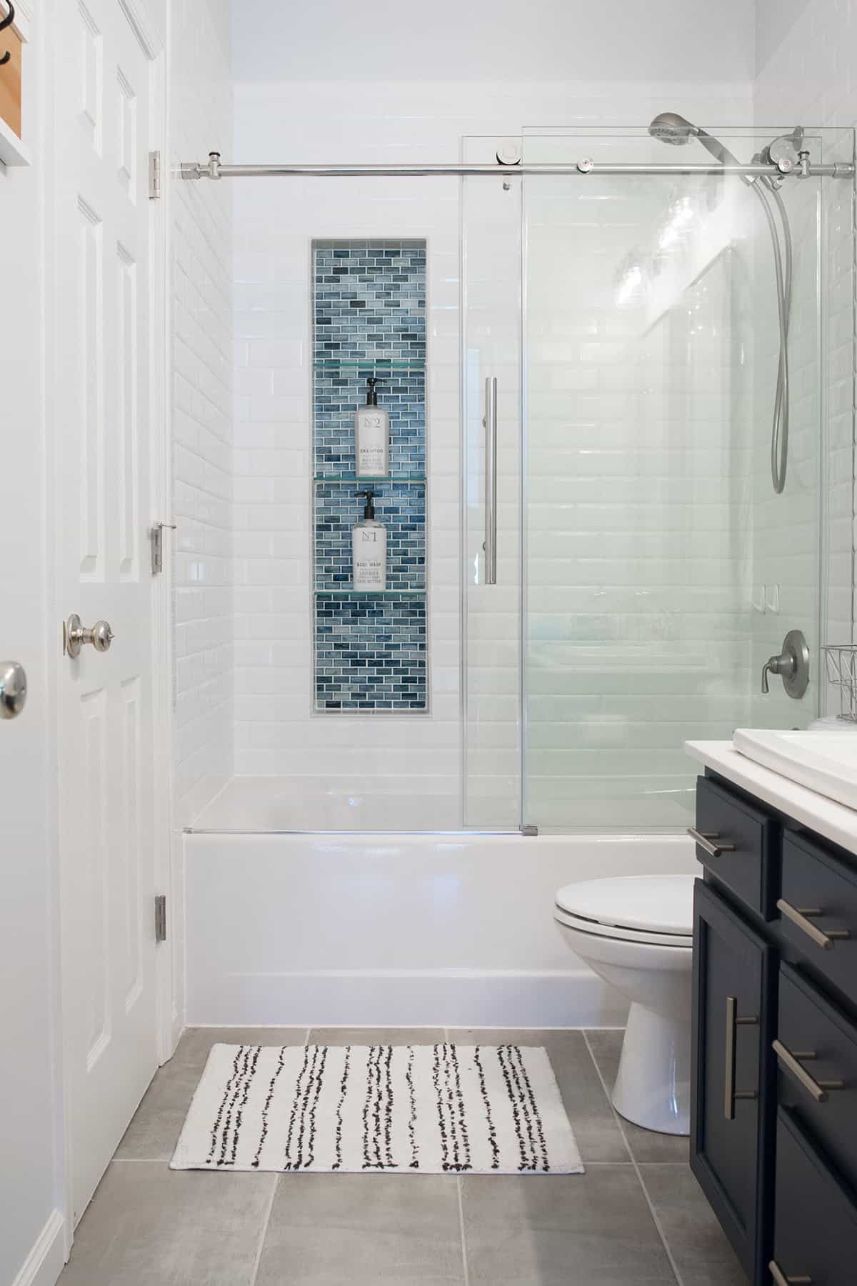 White subway tile in shower with glass door and extra large shower niche in blue tile.